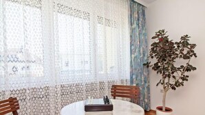 A room with a round table, two wooden chairs, a bench, a potted plant, and patterned curtains.