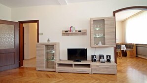 A modern living room with a wooden herringbone floor, a built-in entertainment unit with a flat-screen TV, speakers, and glass-fronted shelving.