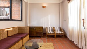 A room with a glass coffee table, wicker sofa, striped armchair, and a wooden chest of drawers. - Team Yala Inn (Lalitpur)