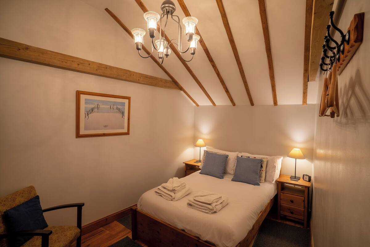 A bedroom with a wooden ceiling, a bed with white linens, two bedside lamps, and a framed picture on the wall.