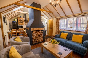 A cozy living room with a fireplace, wooden beams, a sofa, and a dining area. - All Seasons Cottage Breaks (Saxmundham)