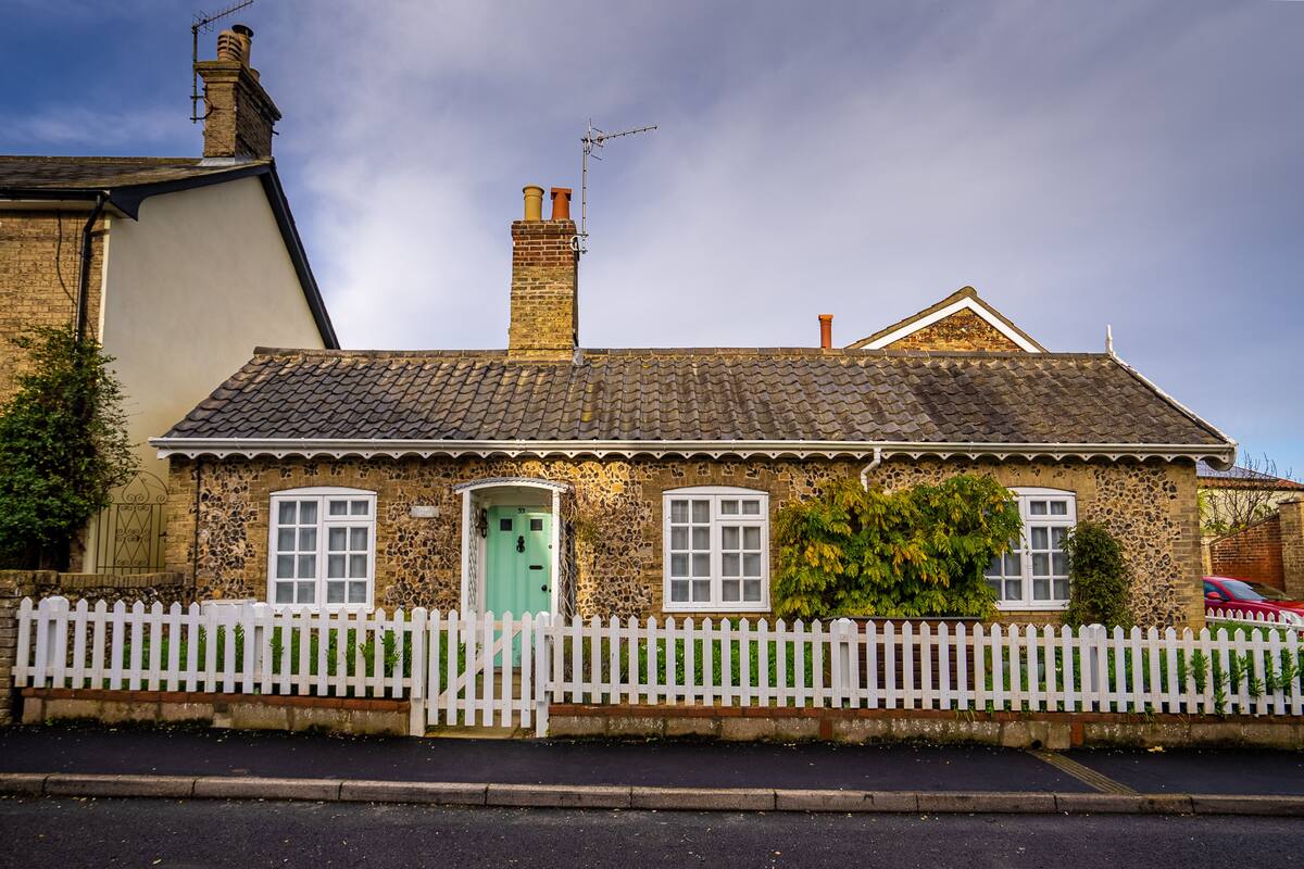 A stone house with a white picket fence, a green door, and a chimney.