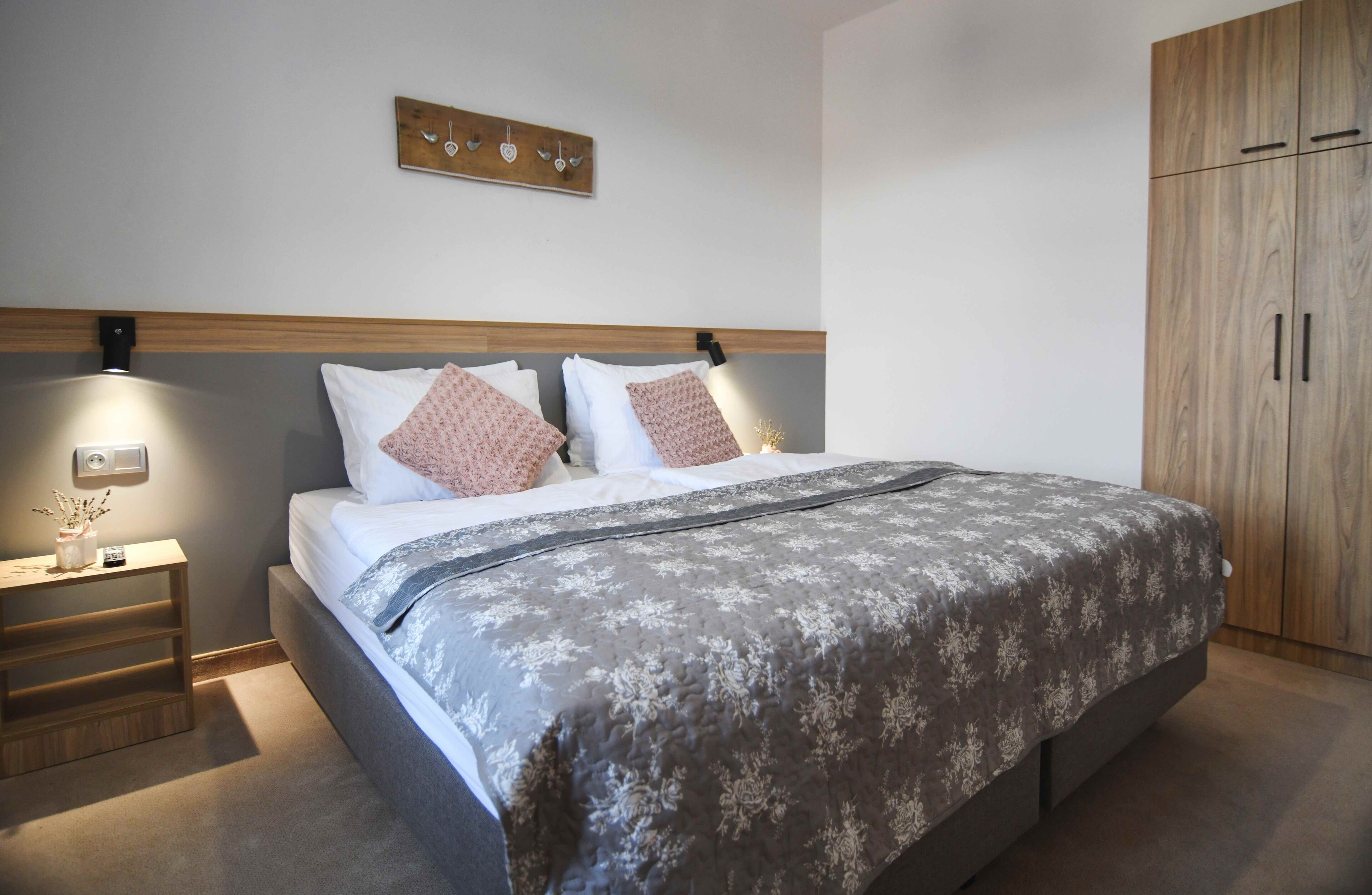 Une chambre à coucher comprenant un lit, des tables de chevet, une commode, une armoire en bois et une œuvre d’art accrochée au mur.