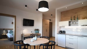 Una cocina moderna con armarios blancos, encimera de madera y horno empotrado. Hay una zona de comedor con una mesa redonda y sillas negras.
