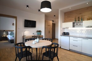 A modern kitchen with white cabinets, a wooden countertop, and a built-in oven. There is a dining area with a round table and black chairs. - Dworzysko Hotel & Restaurant (Szczawno-Zdroj)