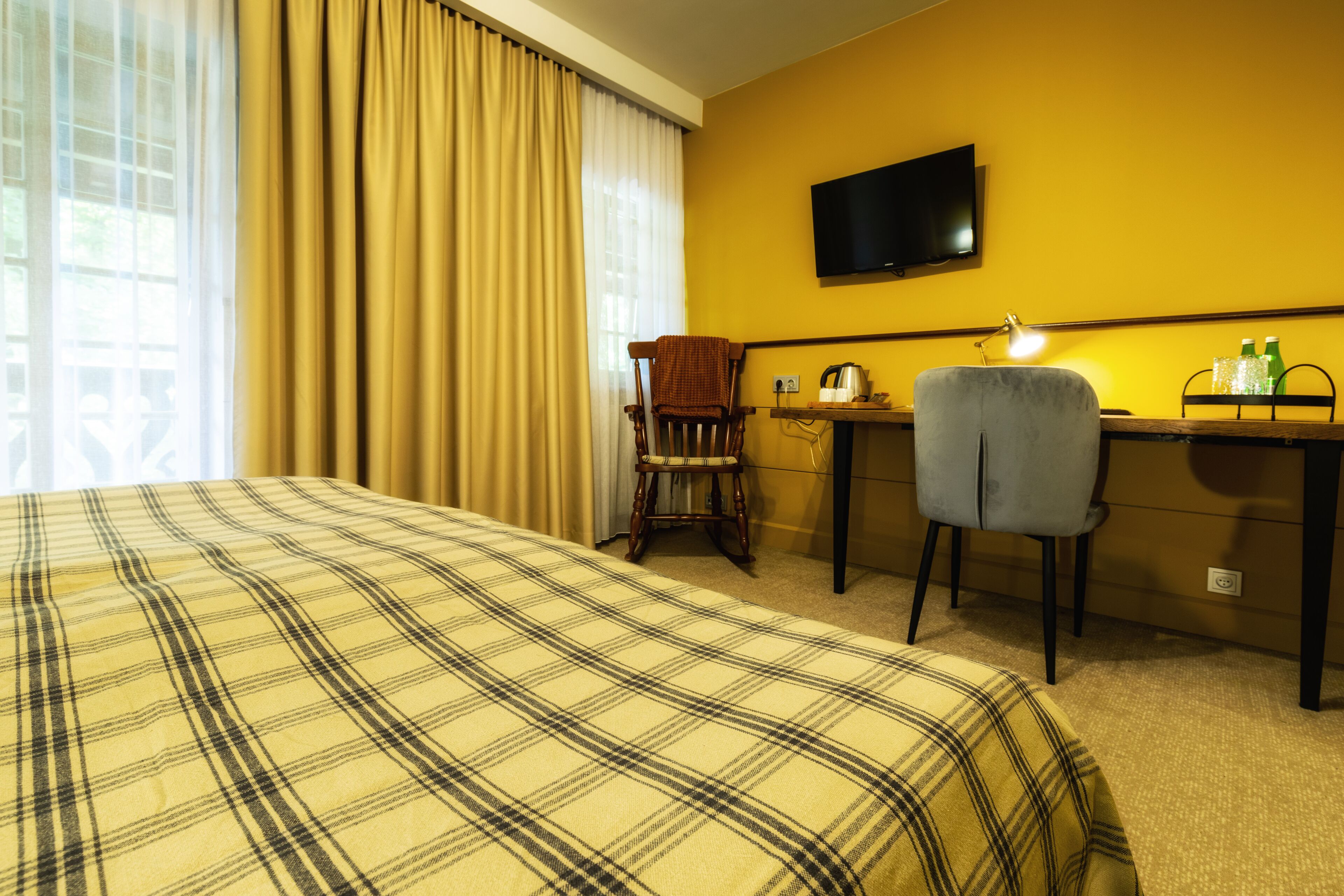 A hotel room with a bed, a desk, a chair, a television, and a window with curtains.