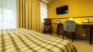 A hotel room with a bed, a desk, a chair, a television, and a window with curtains.