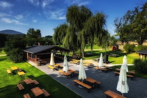 An outdoor seating area with tables and umbrellas, surrounded by trees and a building with a sign that reads 'FOOD GRILL'. - Dworzysko Hotel & Restaurant (Szczawno-Zdroj)