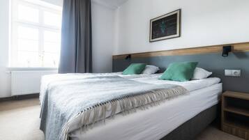 Habitación de hotel con una cama grande, cabecera, mesita de noche y un cuadro en la pared. Incluye una ventana con cortinas.