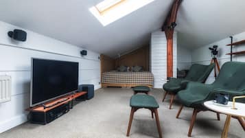 Un dormitorio estilo loft moderno con una cama grande, televisor y zona de estar con sillas y otomanas.