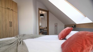 Un dormitorio con techo inclinado, una cama con almohadillas rojas y blancas, un armario de madera y un tragaluz.