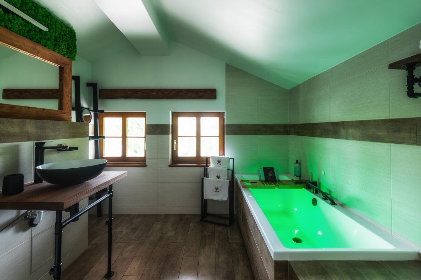 Une salle de bain dotée d’une grande baignoire, d’un meuble-lavabo en bois avec un vasque et de deux fenêtres.