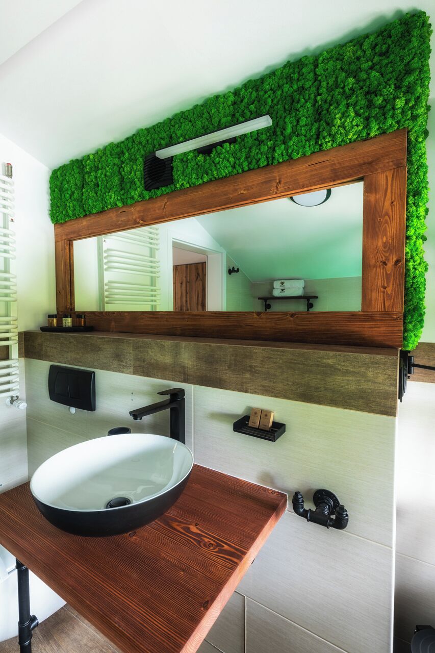 Un baño con tocador de madera, un lavabo blanco y un espejo con una planta en la pared.