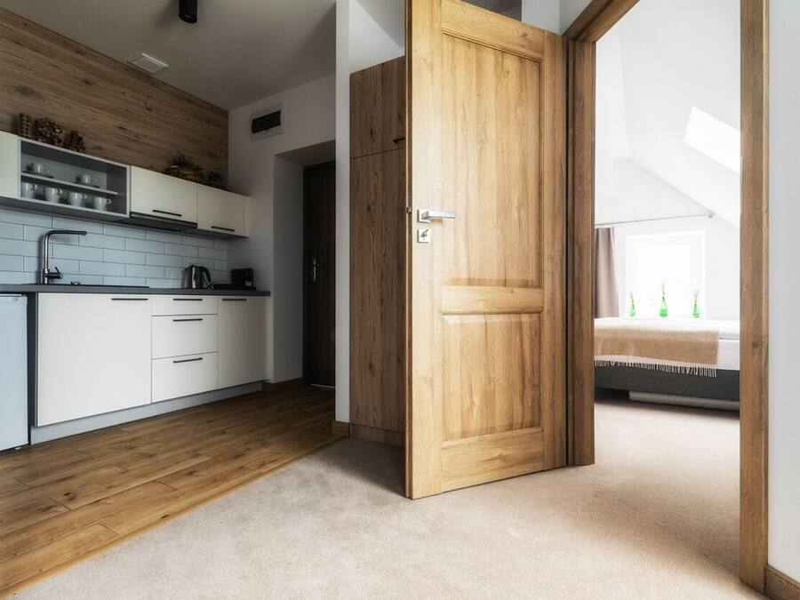 A modern kitchen with white cabinets, a wooden floor, and a large wooden door leading to another room.