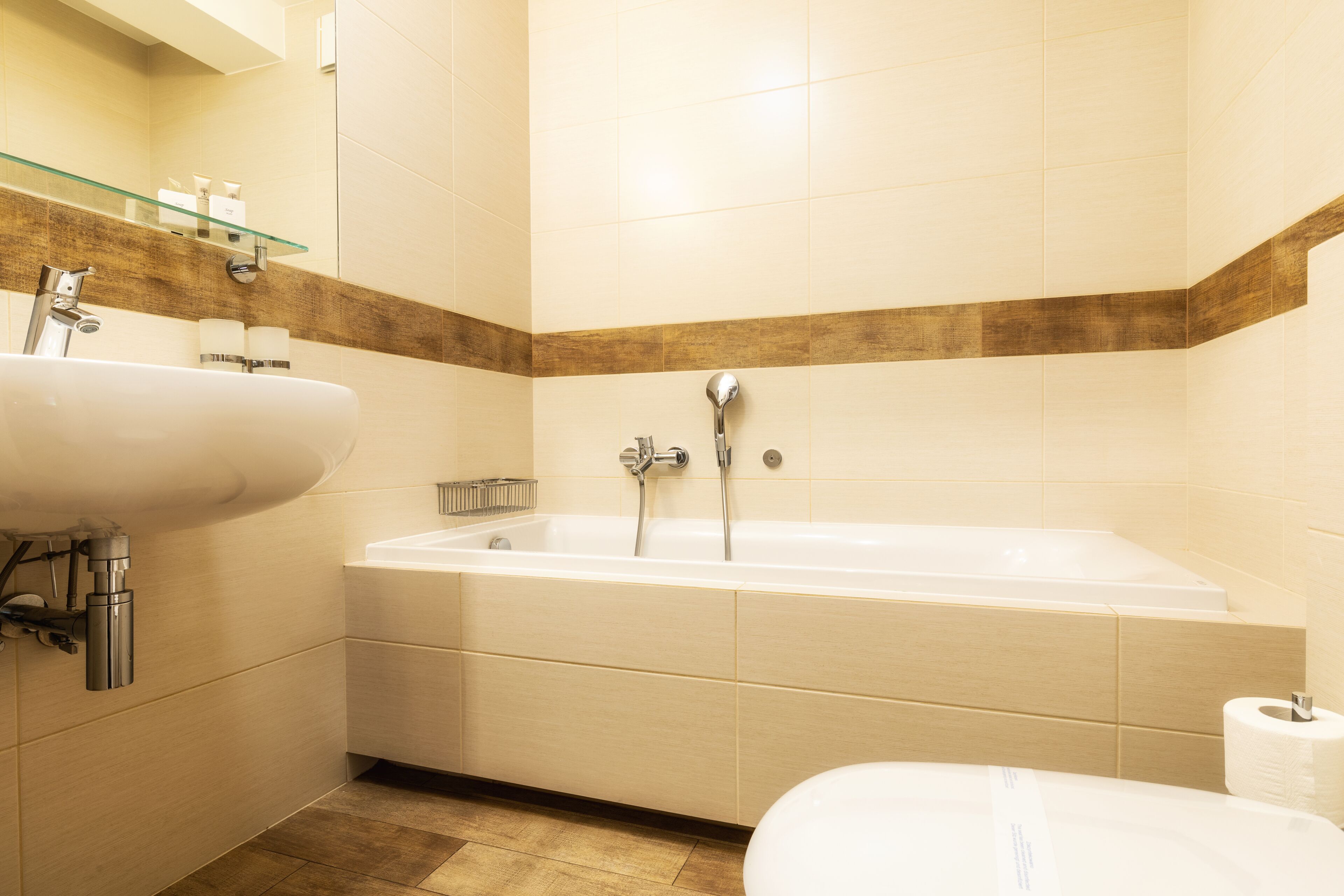 A modern bathroom with a bathtub, two sinks, and a glass shelf with toiletries.
