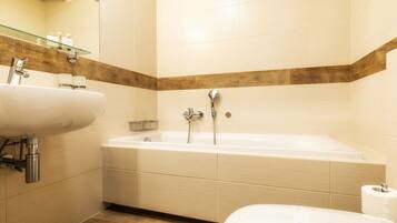 A modern bathroom with a bathtub, two sinks, and a glass shelf with toiletries.