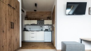 Una cocina moderna con armarios blancos, piso de madera y un reposapiés gris.