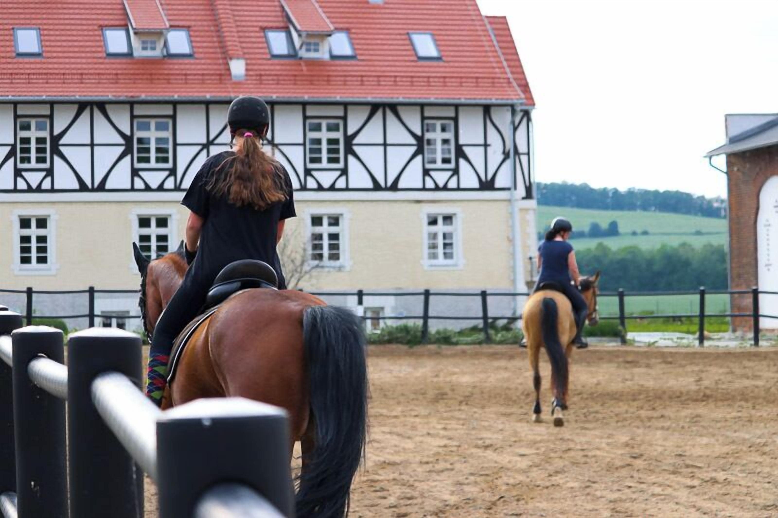 Un manège où l’on peut faire de l’équitation, avec un bâtiment traditionnel en arrière-plan.