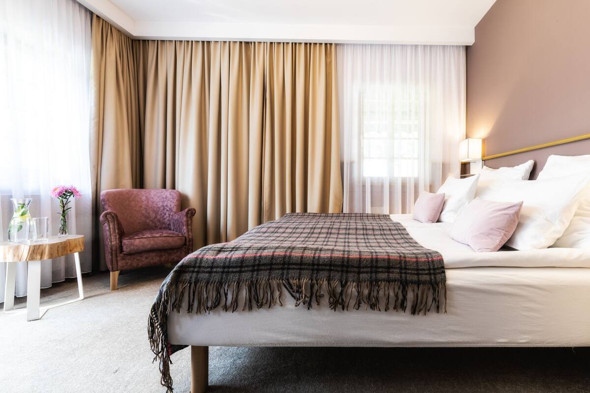 A hotel room with a bed, a chair, a small table, and a lamp.