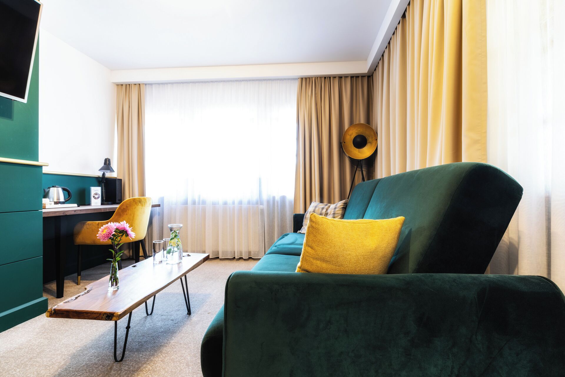 Uma sala de estar moderna com um sofá verde, um travesseiro amarelo, uma mesa de centro de madeira e uma cadeira amarela.