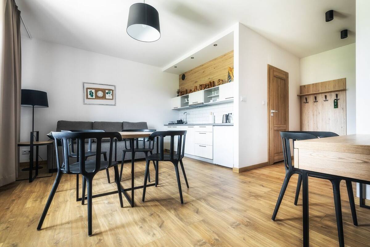 A modern kitchen with white cabinets, a wooden countertop, and a dining area with a wooden table and black chairs.