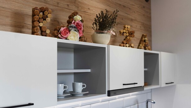 Una cocina con armarios blancos, pared de madera y detalles decorativos como flores y un florero.
