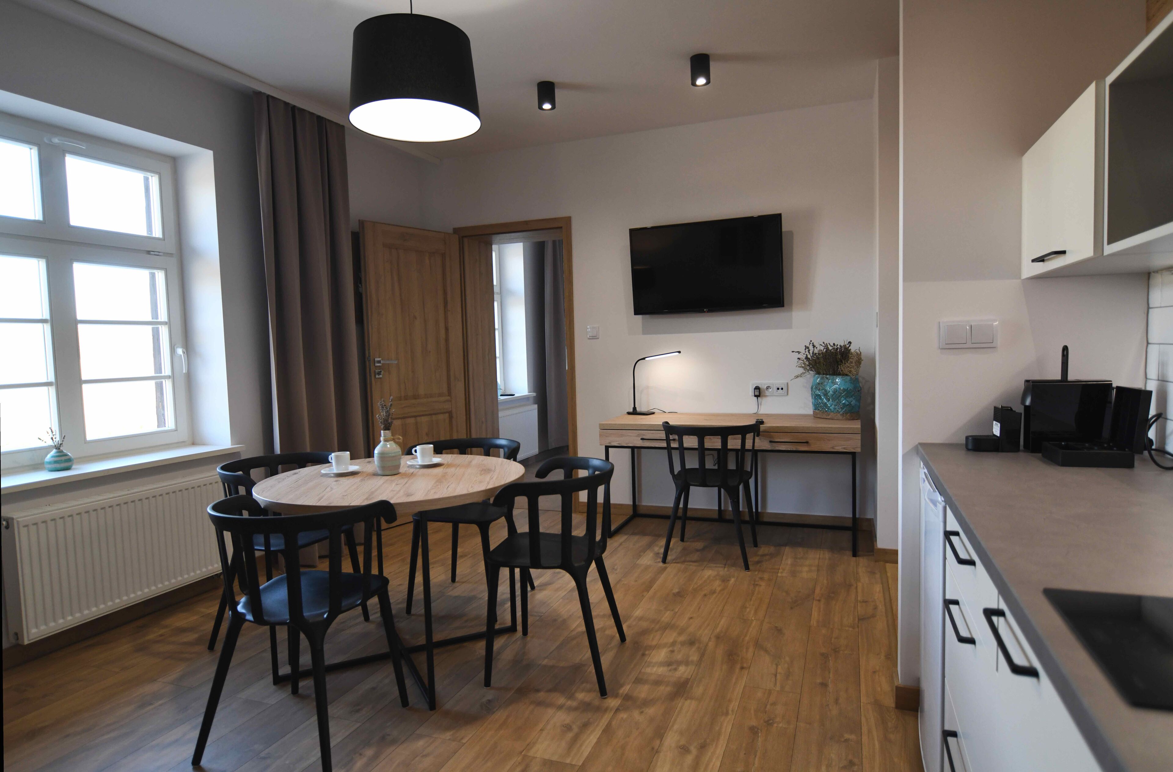 A modern kitchen with a wooden dining table, chairs, and a TV mounted above the counter.