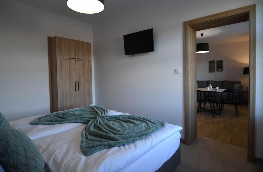A bedroom with a bed, a wardrobe, a television, and a dining area visible through an open doorway.