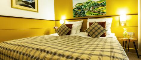 A hotel room with a large bed, a painting on the wall, and two wall-mounted lamps.