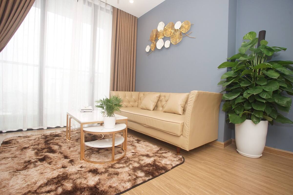 Ein modernes Wohnzimmer mit einem beige gefärbten Sofa, einem weißen Couchtisch, einer großen Topfpflanze und einem Wandbild.