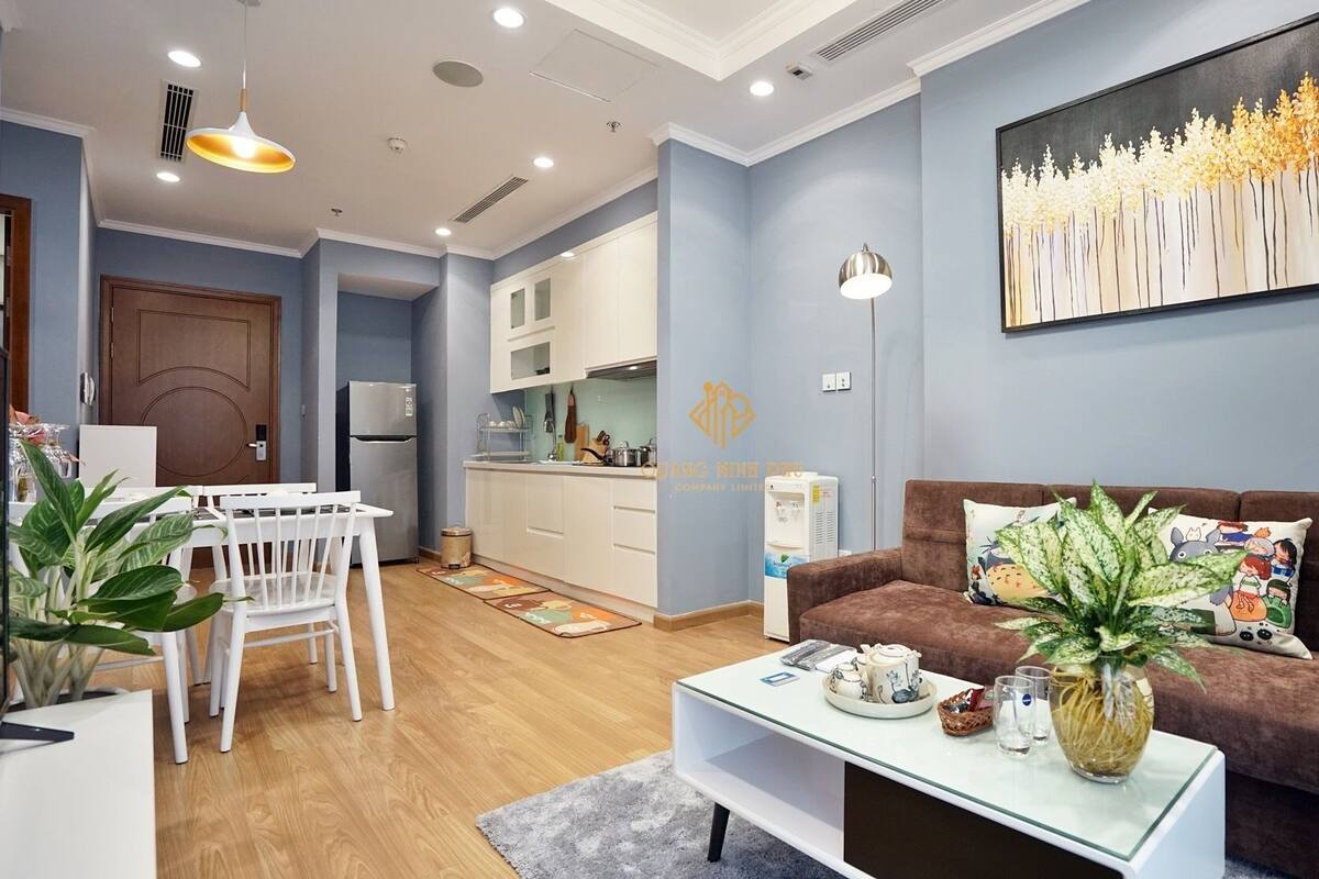 Ein modernes Wohnzimmer mit einem braunen Sofa, einem Essbereich mit weißem Tisch und Stühlen sowie einer Küche im Hintergrund.