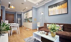 A modern living room with a brown sofa, a dining area with a white table and chairs, and a kitchen in the background.