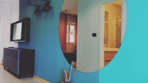 A modern interior with a blue wall, a black entertainment unit, and a mirror reflecting a room with a wooden floor. - Apartments Pržina (Lumbarda)