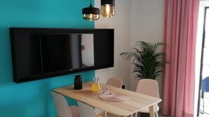 A modern dining area with a teal wall, a flat-screen TV mounted above a wooden table, and pink curtains. - Apartments Pržina (Lumbarda)