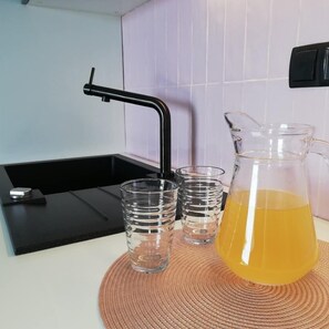 A kitchen with a black faucet, three clear glasses, and a pitcher of yellow liquid on a woven mat.