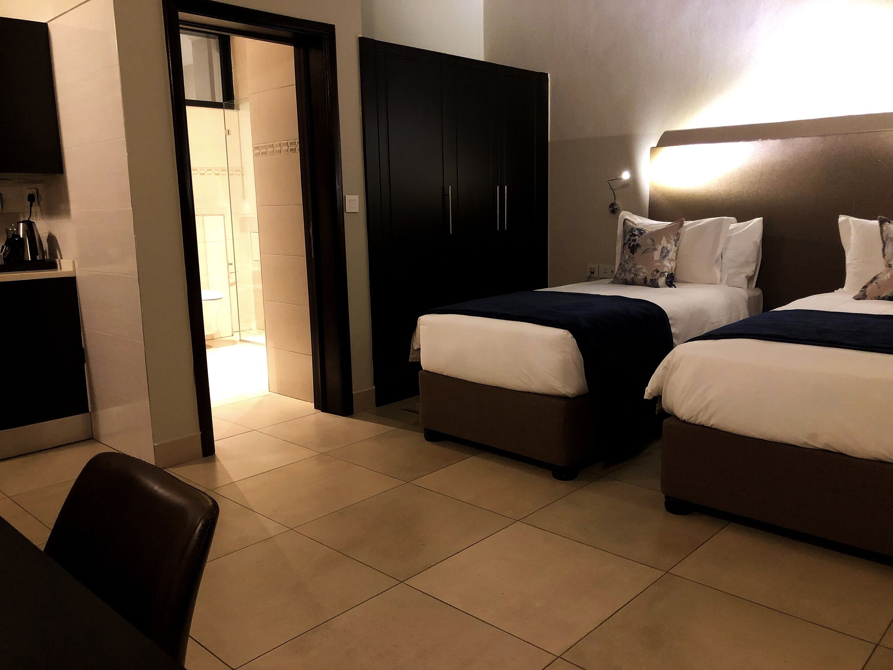 Een hotelkamer met twee bedden, een bureau en een stoel. Er is een deur naar een badkamer.
