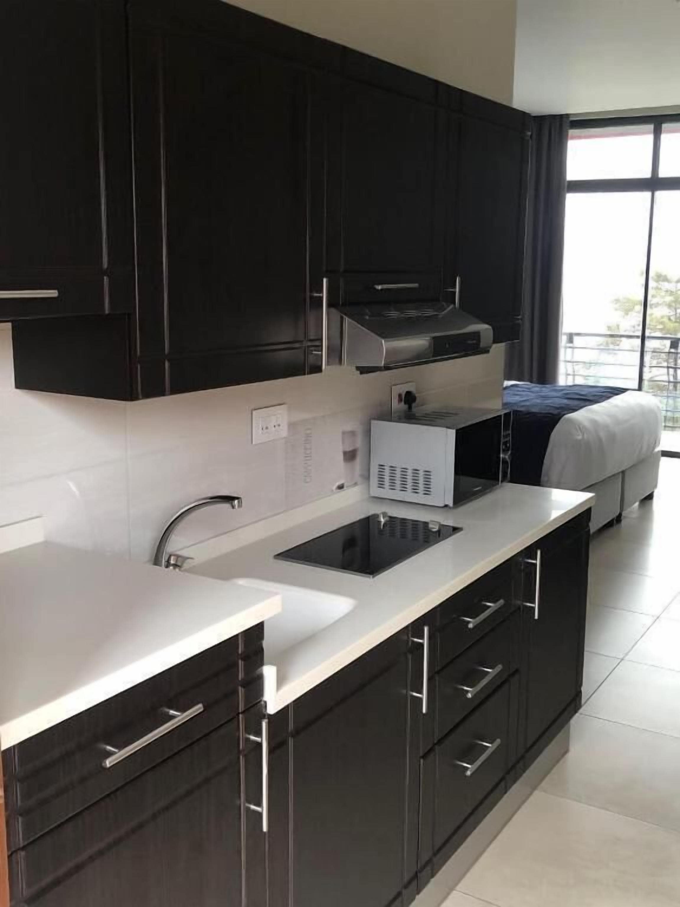 A modern kitchen with dark cabinets, a white countertop, a built-in stove, and a window with a view of the outdoors.