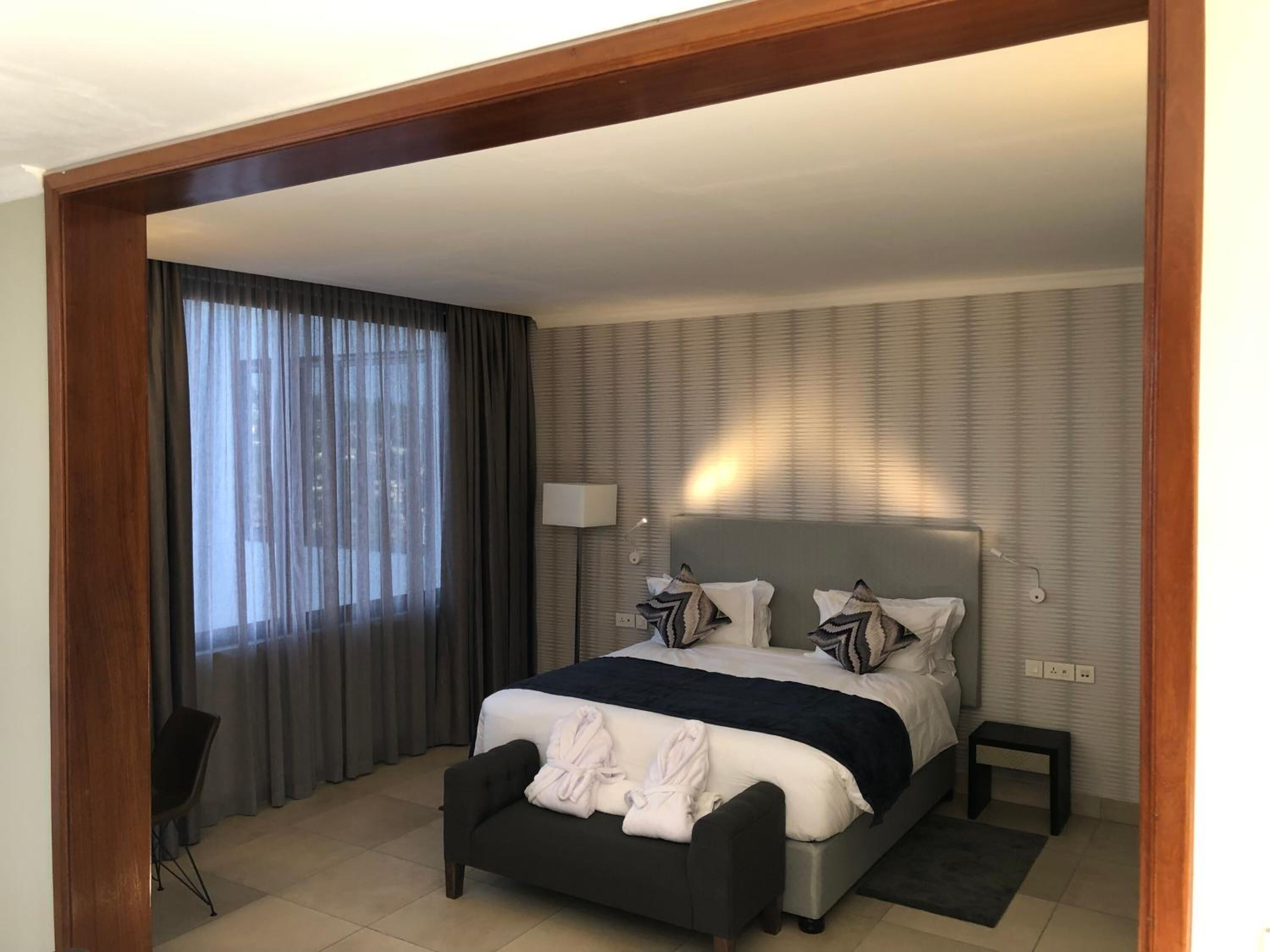 Habitación de hotel moderna con una cama grande, una mesita de noche, una lámpara y vistas a la ciudad por la ventana.