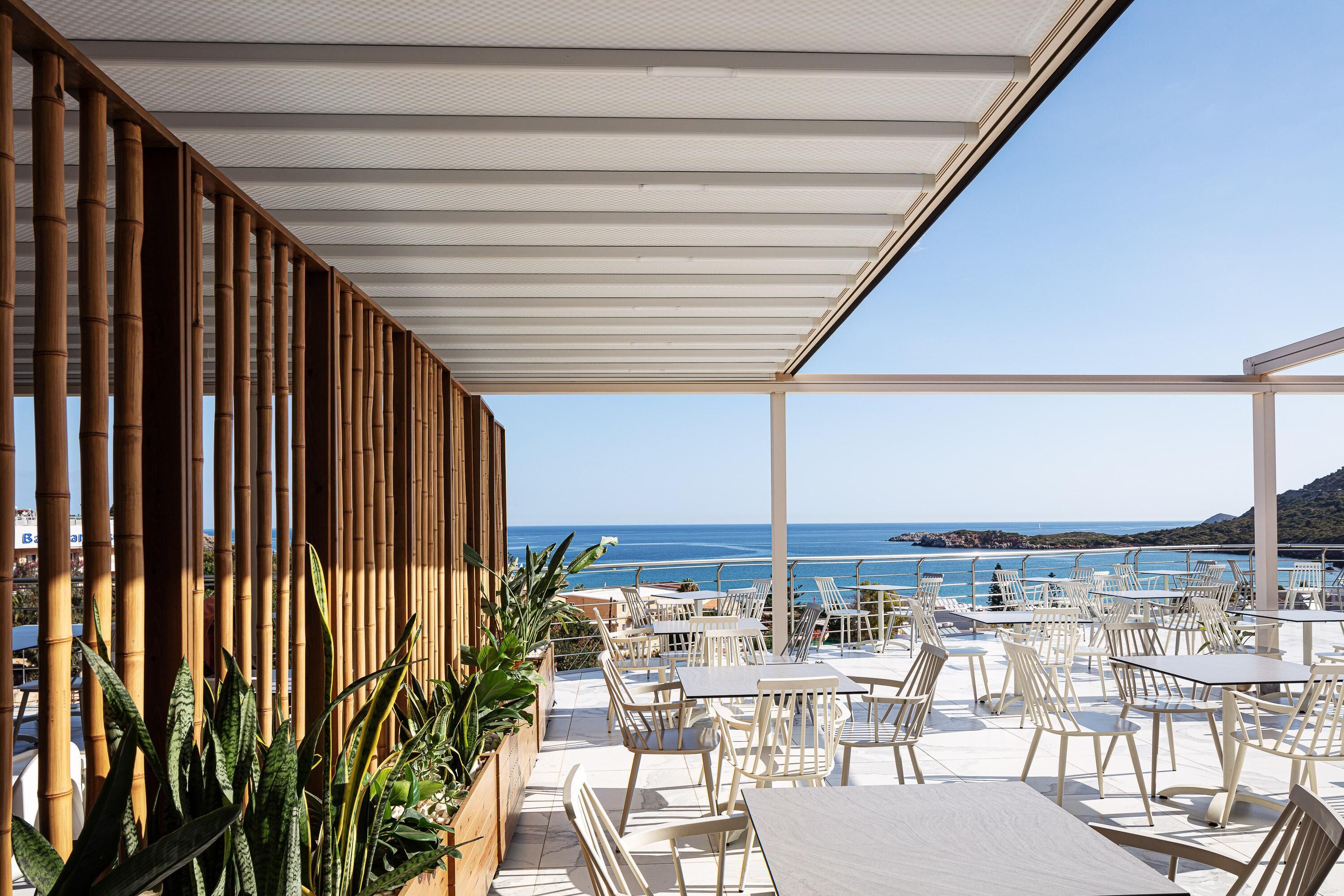 An outdoor terrace with tables and chairs, bamboo columns, and a view of the sea.