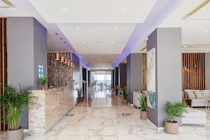 Un hall d’hôtel moderne avec un comptoir d’accueil en marbre, un espace salon et une vue sur l’extérieur.
