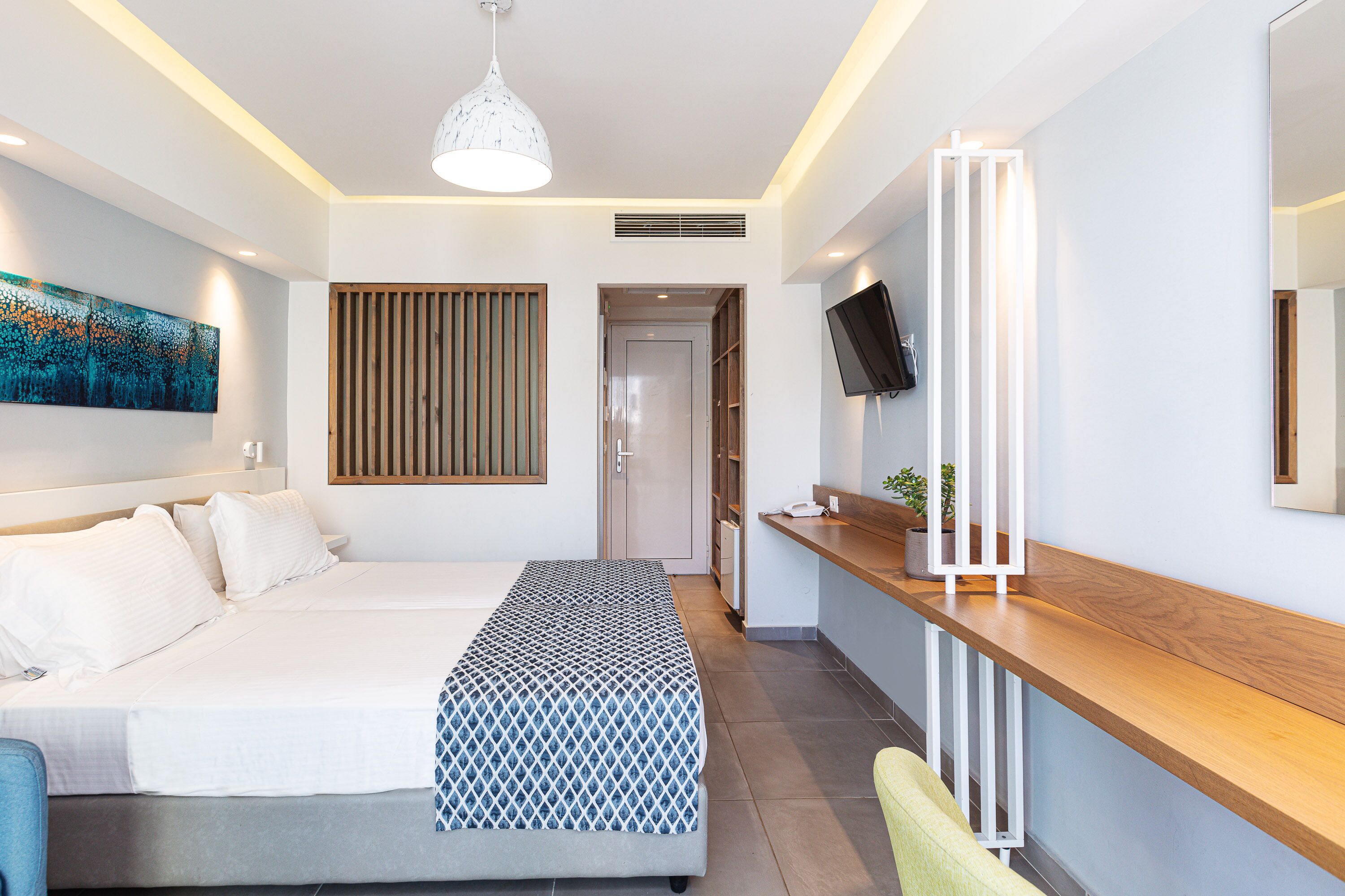 A modern hotel room with a bed, bedside table, TV, and artwork on the wall.