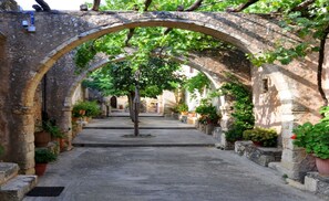 Un chemin en pierre en forme d’arche, dans un bâtiment historique, agrémenté de plantes en pot et d’un arbre au centre.