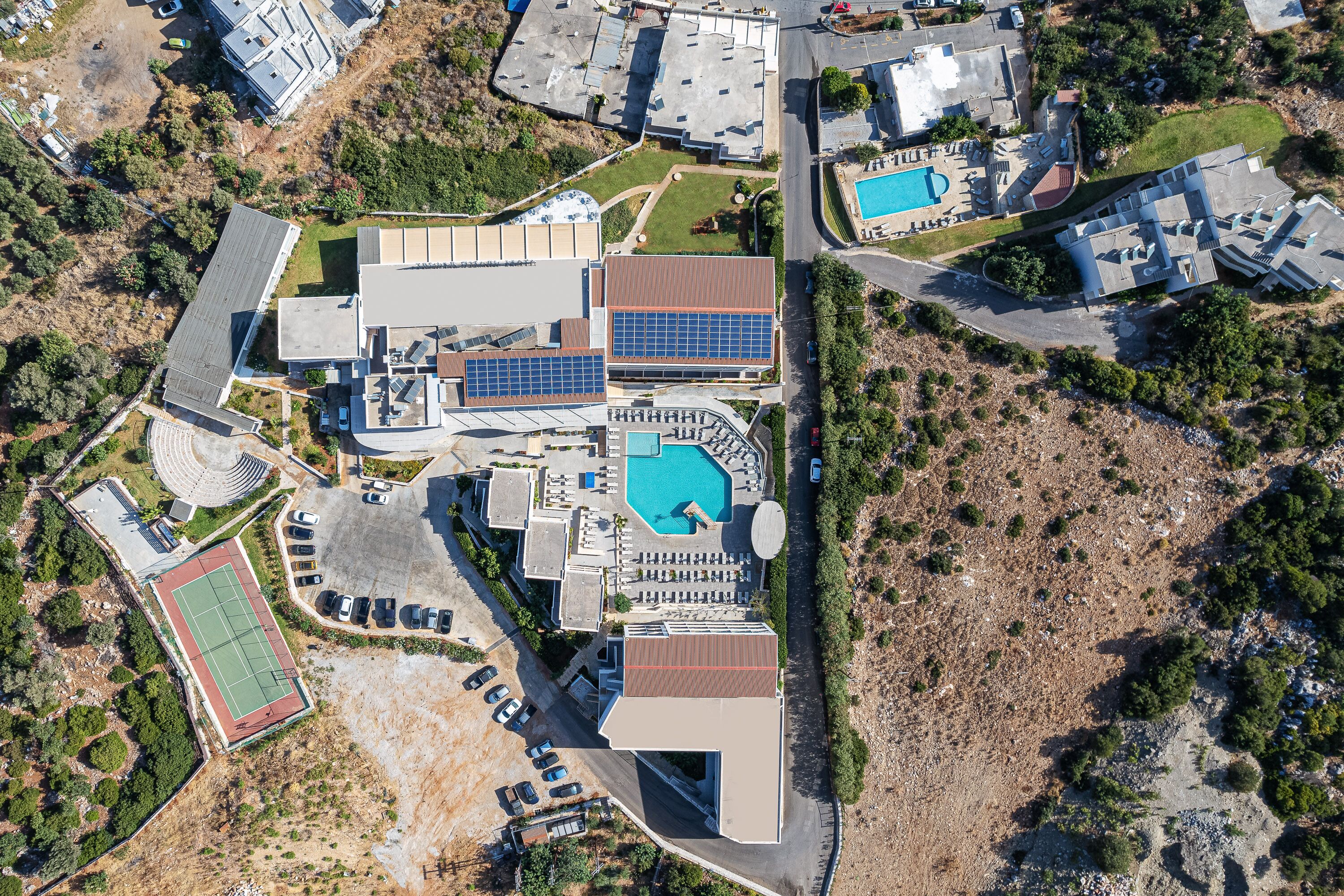 Vista aérea de una zona residencial con varios edificios, una piscina y una cancha de tenis.