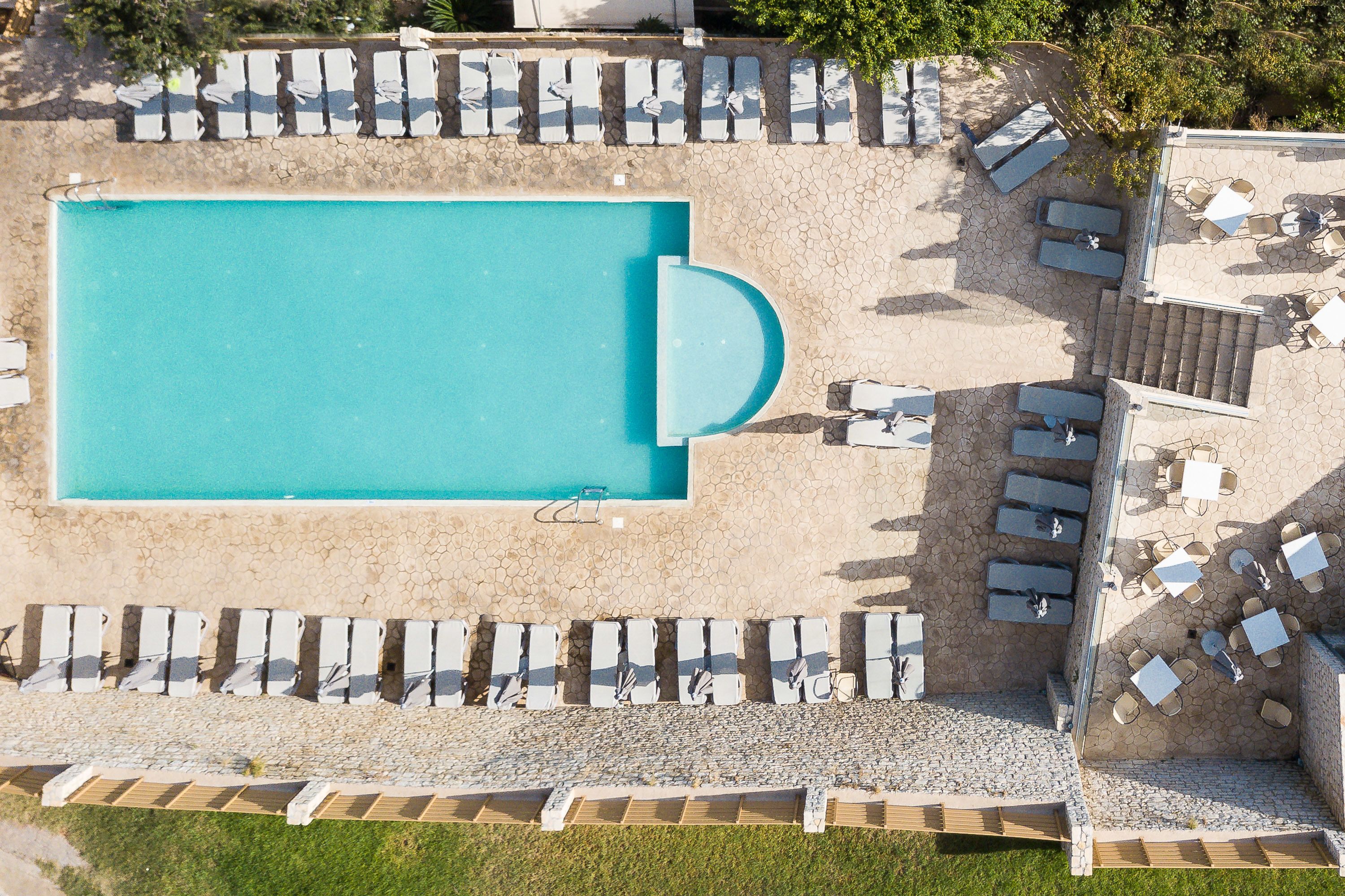 An aerial view of a swimming pool with adjacent lounge areas and a stone-tiled deck.