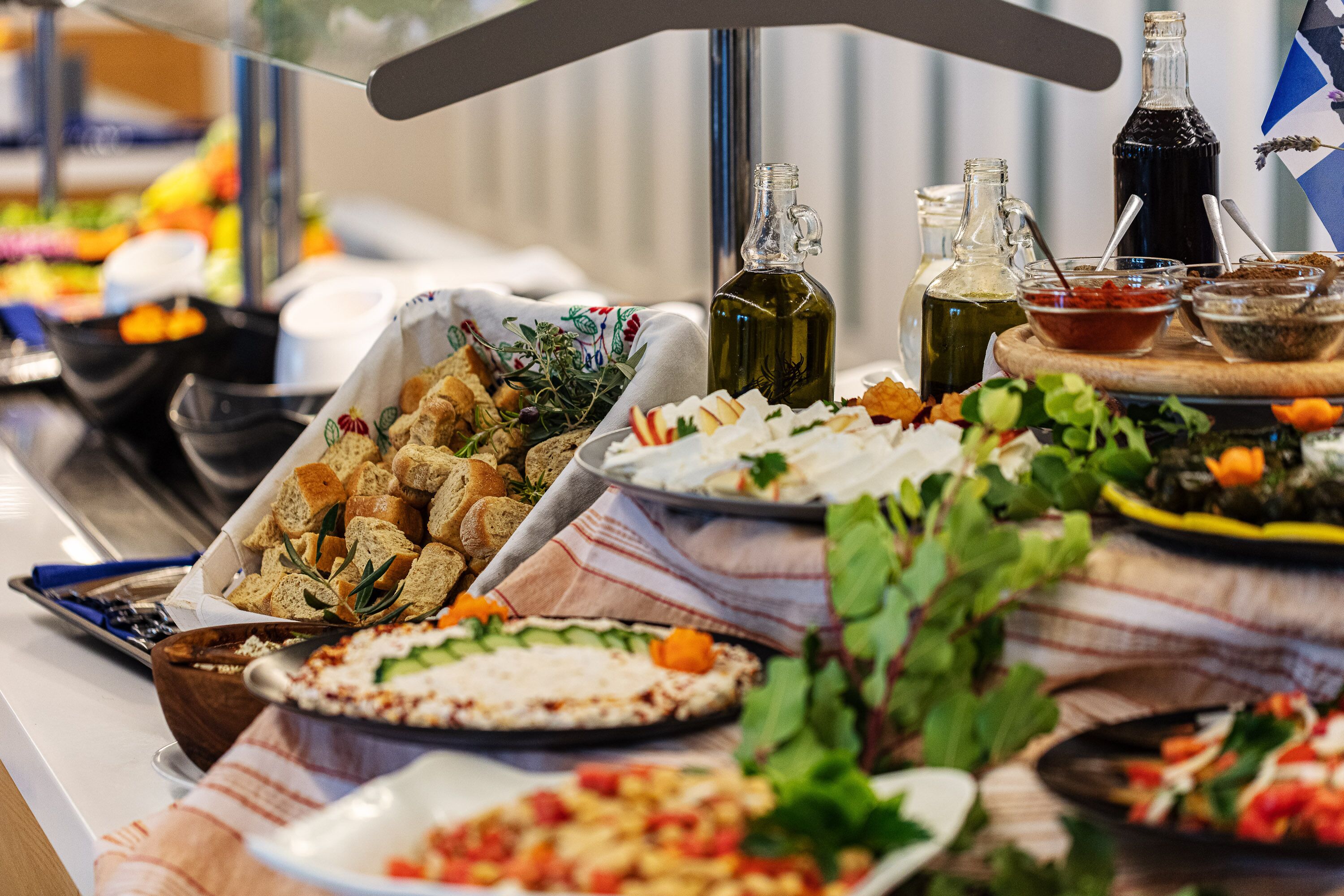 A buffet table with various dishes, including bread, salads, and dips, along with several bottles of sauces.