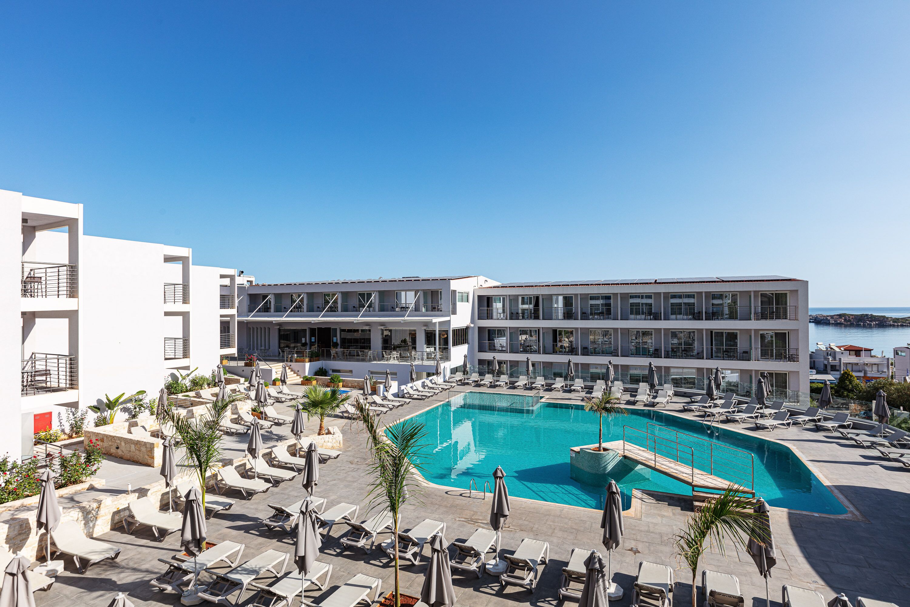 A modern hotel with a large pool, sun loungers, and a view of the sea.