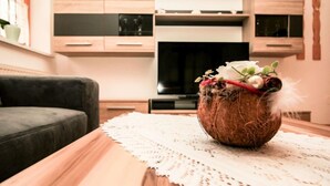 A cozy living room with a dark grey sofa, a wooden coffee table with a lace table runner, and a decorative vase with flowers and greenery. - Apartment Poldi by Interhome (Haus)
