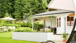 A covered outdoor seating area with a pool, surrounded by lush greenery and a white building with red window frames. - Apartment Poldi by Interhome (Haus)