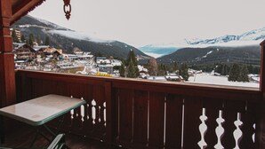 Un balcón de madera con vistas a un paisaje nevado de montañas, una mesa y sillas.