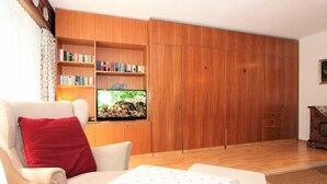 A living room with a sofa, a red pillow, a television, wooden shelves with books, and a wooden wardrobe. - Am Birkenhain by Interhome (Seefeld in Tirol)